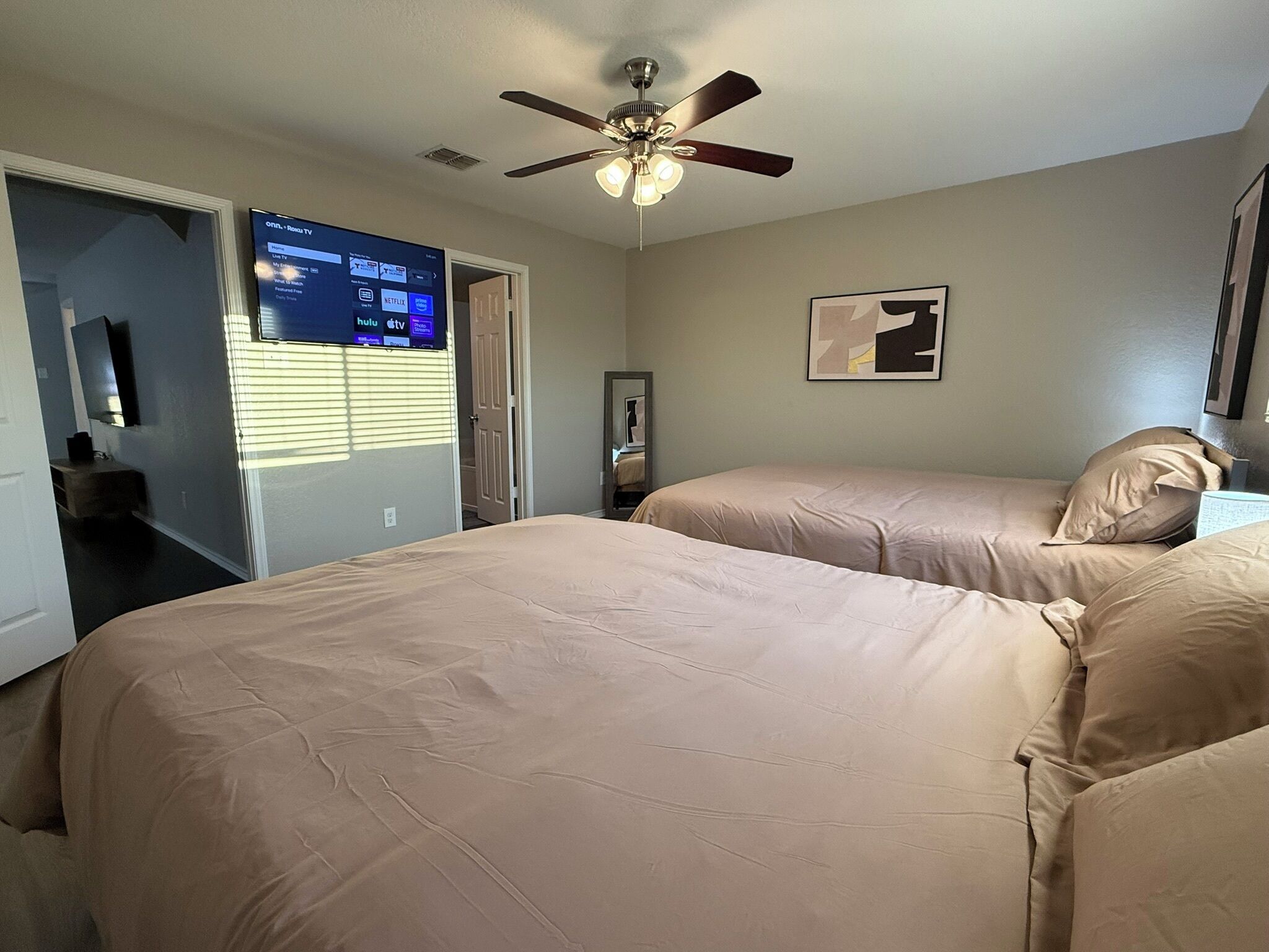 A bedroom with two beds, a ceiling fan, a TV displaying streaming services, and a framed picture on the wall.