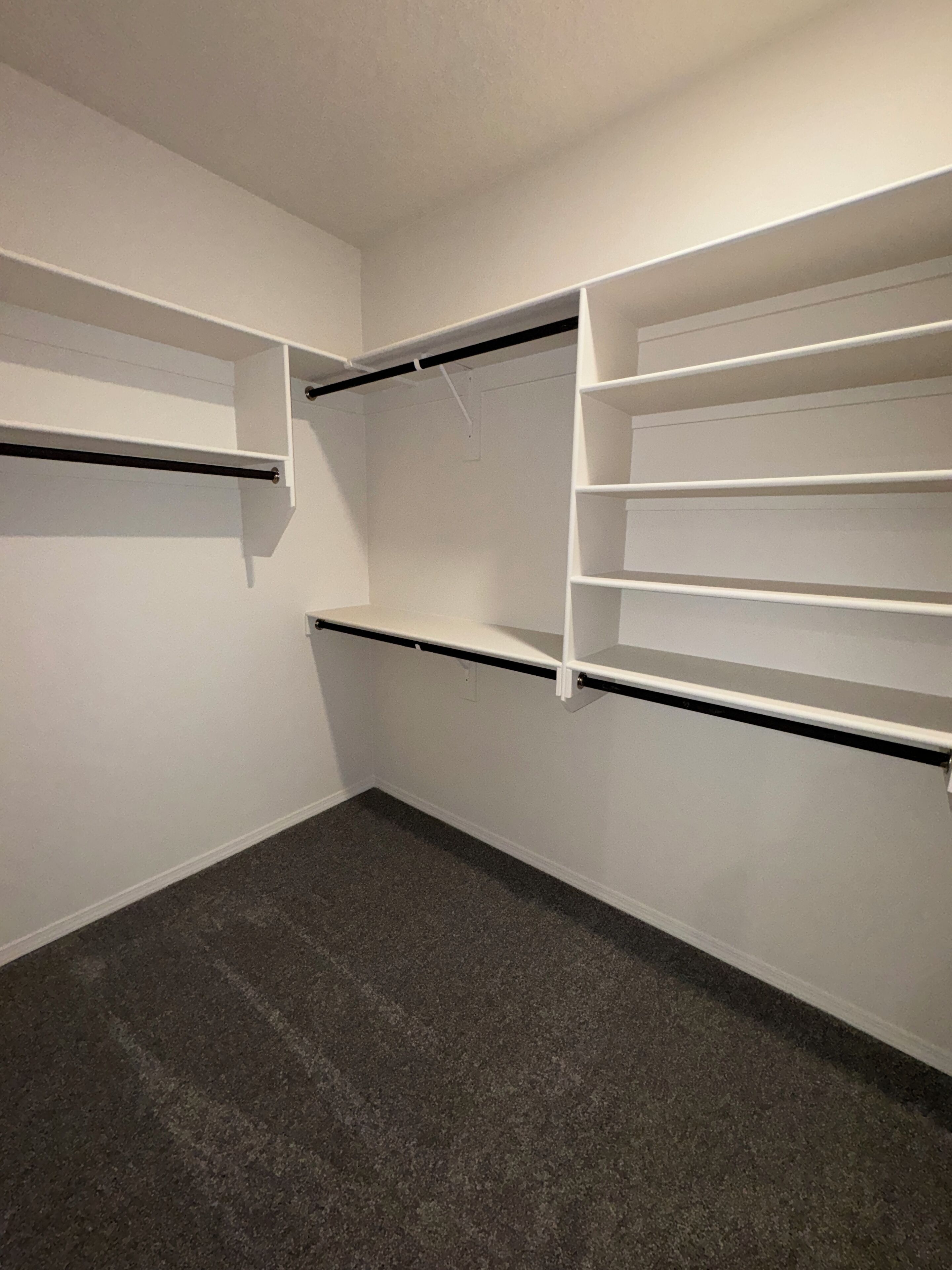 A closet with open shelves and hanging rods, carpeted floor, and white walls.
