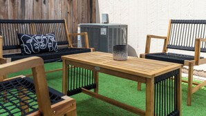 Een houten tafel met een metalen rooster, omringd door vier houten stoelen met zwarte kussens.