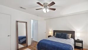 Een slaapkamer met een bed, een plafondventilator, een nachtkastje, een spiegel en een deur.