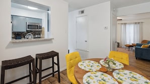 Een moderne woonkamer met een eethoek, een keuken met magnetron en kookplaat, en een blauwe bank.