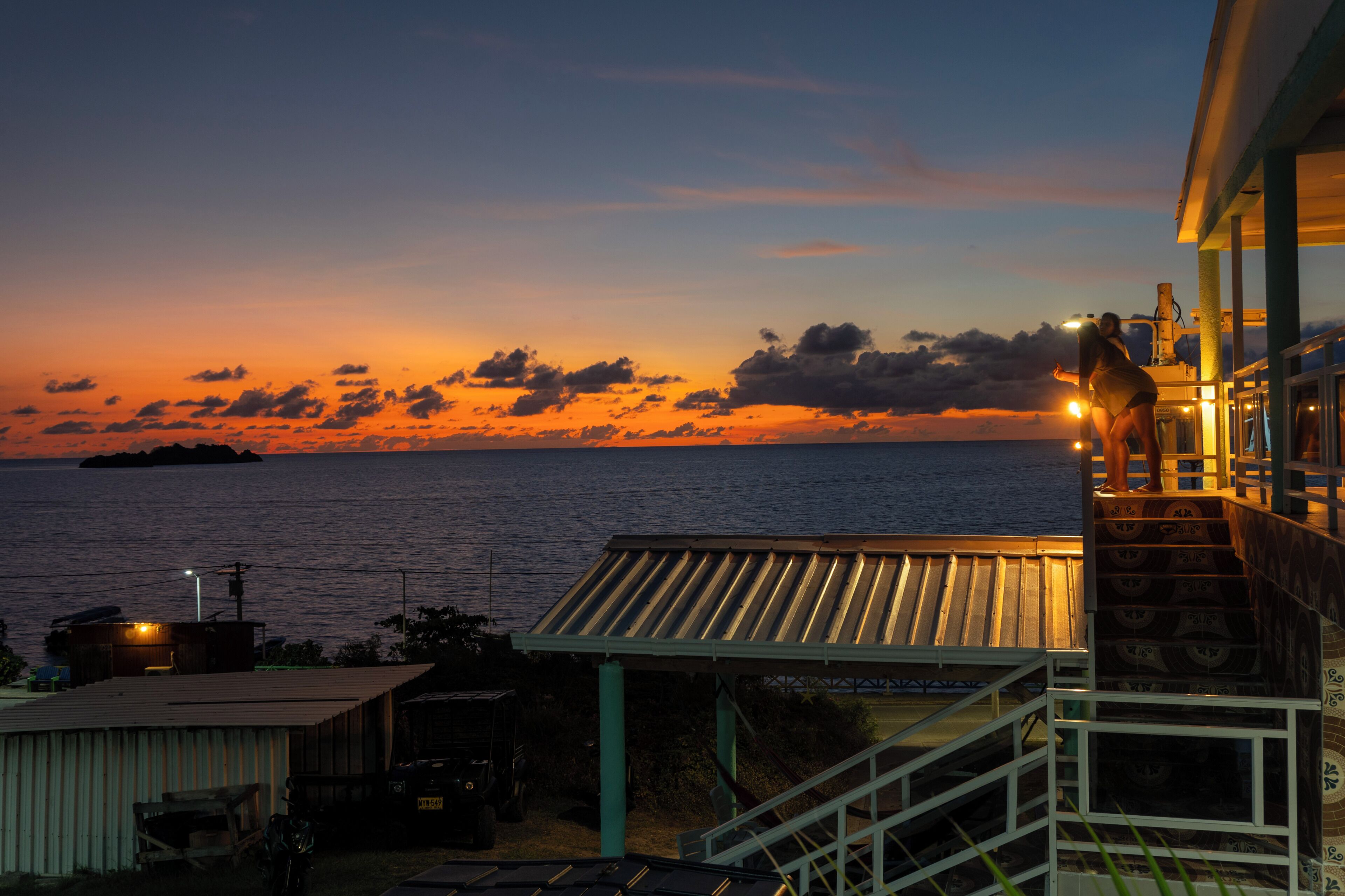 A coastal view with a sunset, a staircase leading to a covered area, and a building with a metal roof.