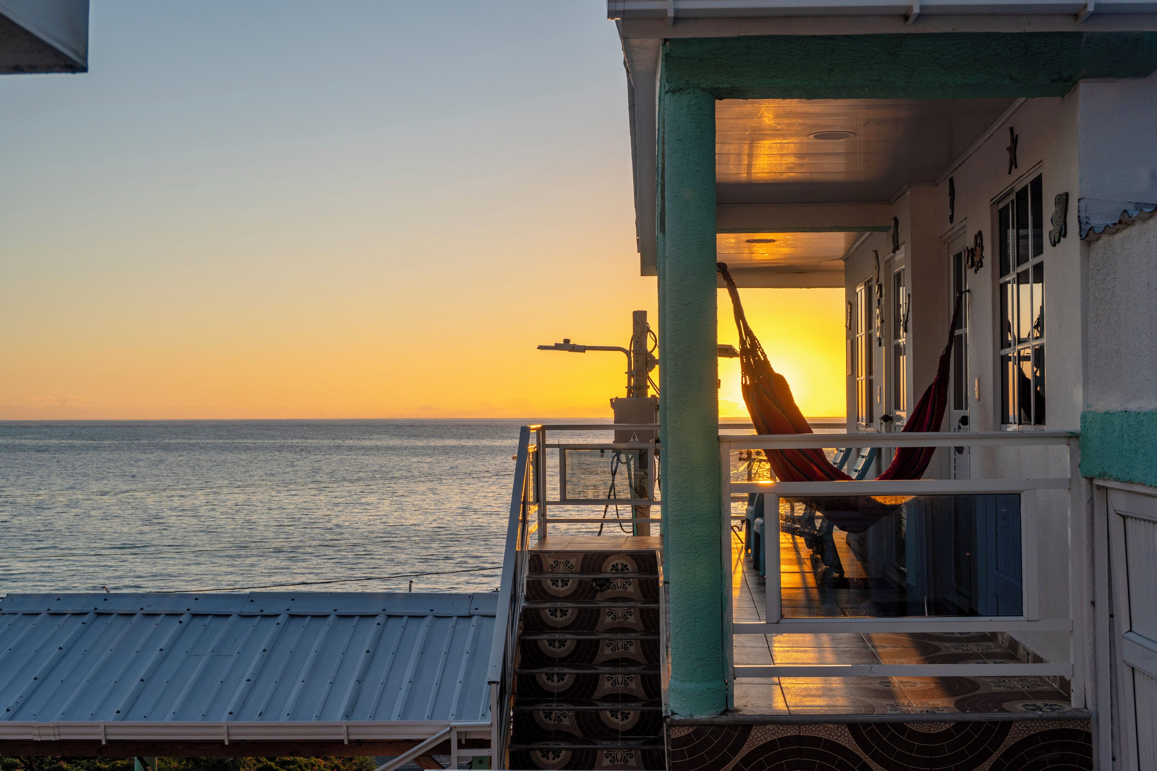 A balcony with a view of the sea at sunset, a hammock, and a railing.