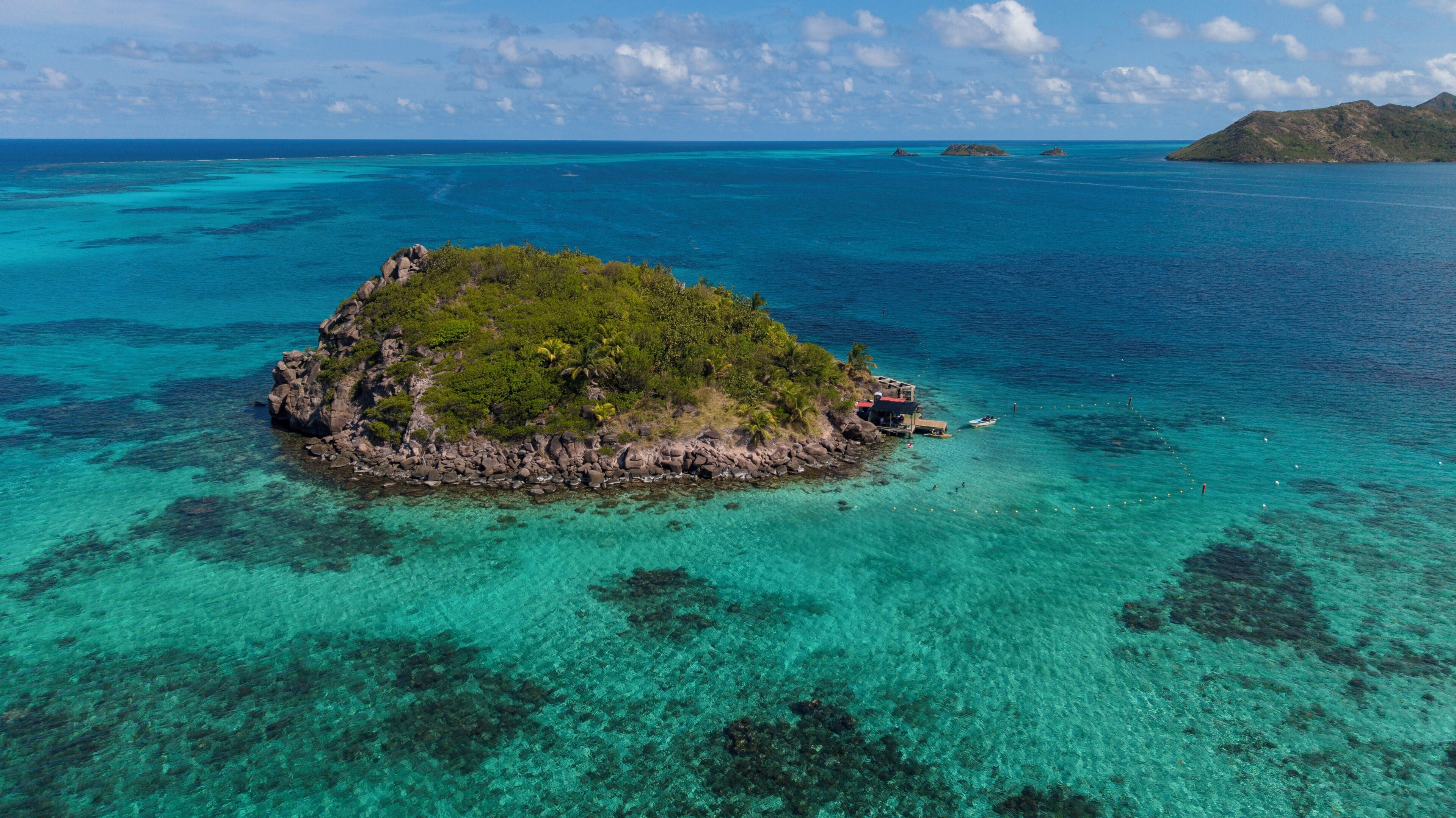 An aerial view of a small island with clear turquoise waters, surrounded by larger landmasses.