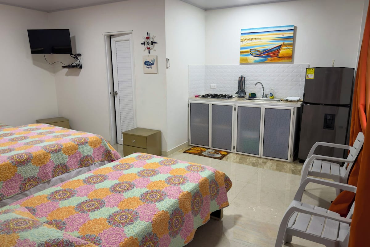 Un dormitorio con dos camas, una kitchenette pequeña, un televisor y un cuadro en la pared.