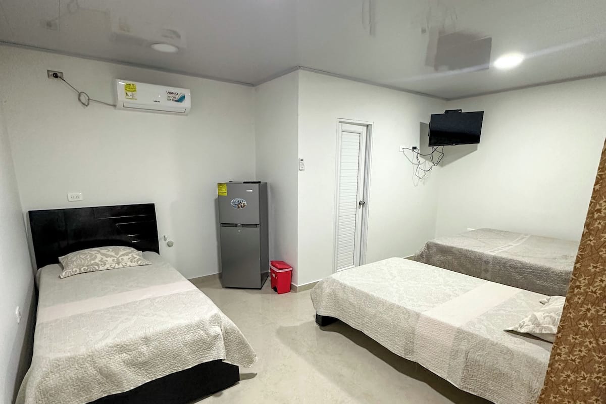 Habitación de hotel con dos camas, un televisor montado en la pared y un ventilador de techo.