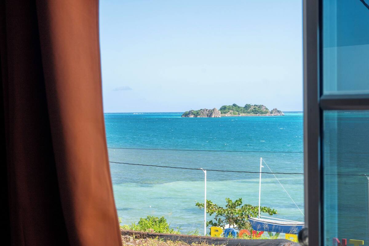 Vista de una zona costera con agua azul cristalina, una pequeña isla y un barco a lo lejos.