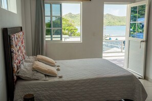 Ένα υπνοδωμάτιο με ένα κρεβάτι, ένα παράθυρο και θέα σε μια έκταση νερού και σε λόφους.