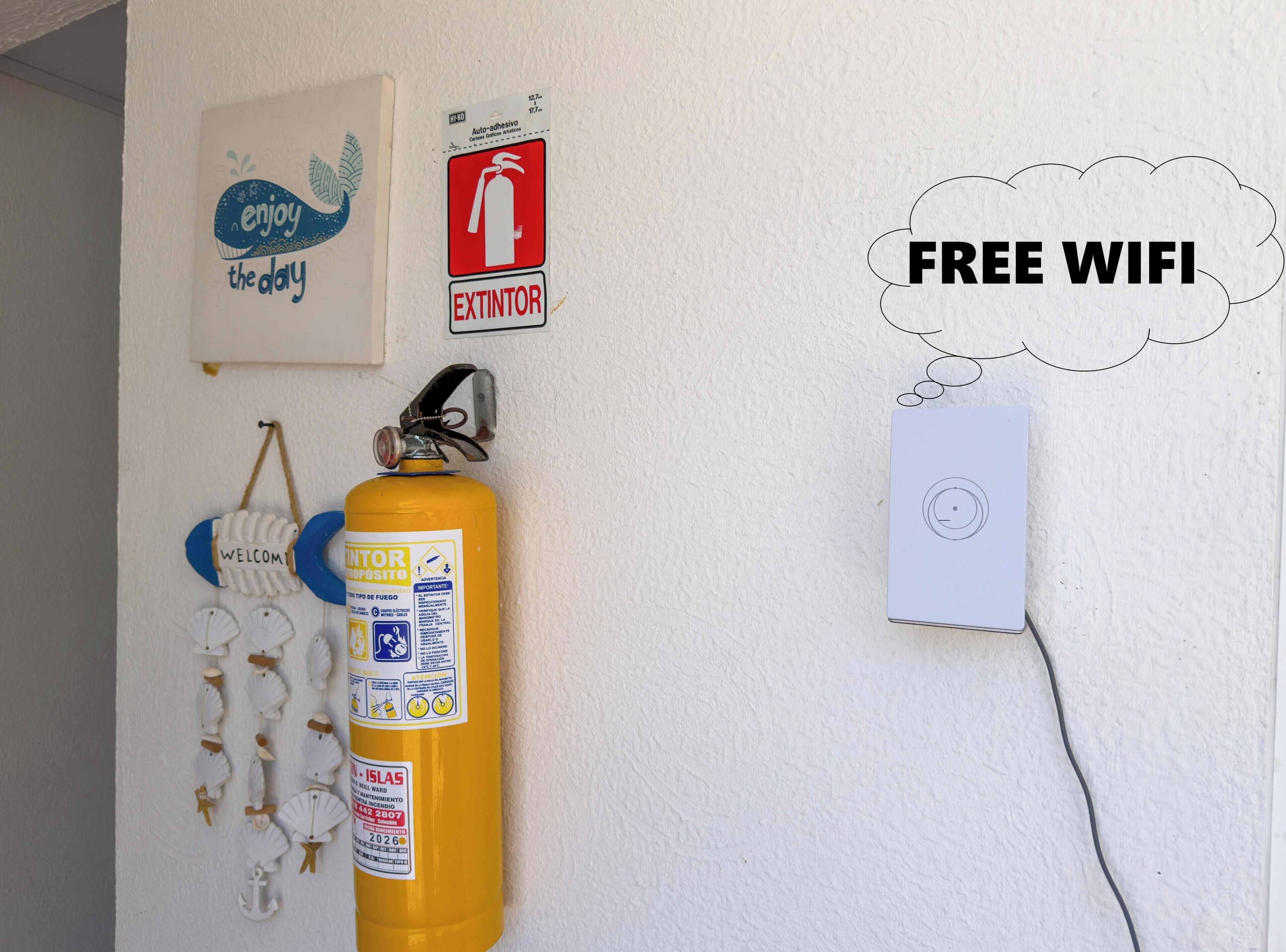 Una pared con un extintor, un cartel de bienvenida, un letrero que indica wifi gratuito y un enchufe.