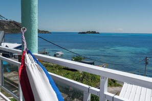 A balcony with a view of the sea, a hammock, and a flag. - Posada Three Cay Suites (Providencia)