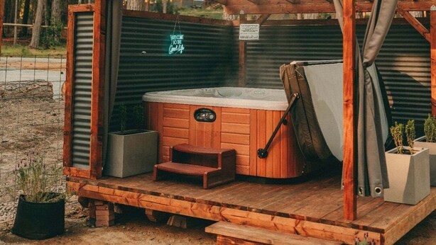 Una cabaña de madera con un jacuzzi, rodeada por una terraza de madera y plantas en macetas.