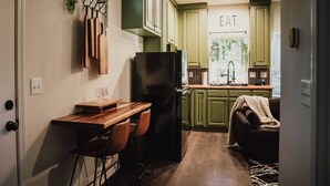 Una cocina compacta con gabinetes verdes, un refrigerador negro, una barra de madera y un rincón de descanso acogedor con una manta.