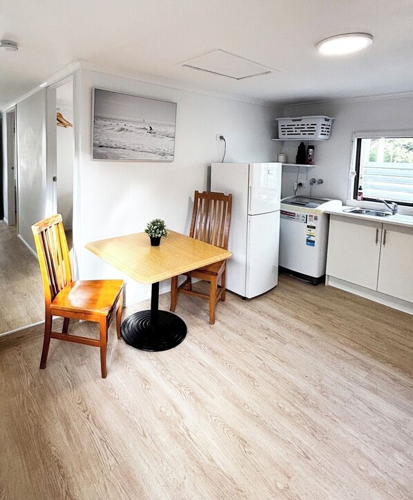 A compact kitchen with a dining table, chairs, a refrigerator, and a window.