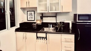A kitchen with white cabinets, a black countertop, a sink, a microwave, and a kettle. - BGC - Fort Mckinley Condo (Taguig)