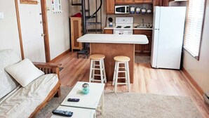 Een compacte keuken met een centraal eiland, houten kastjes, een magnetron en een koelkast.