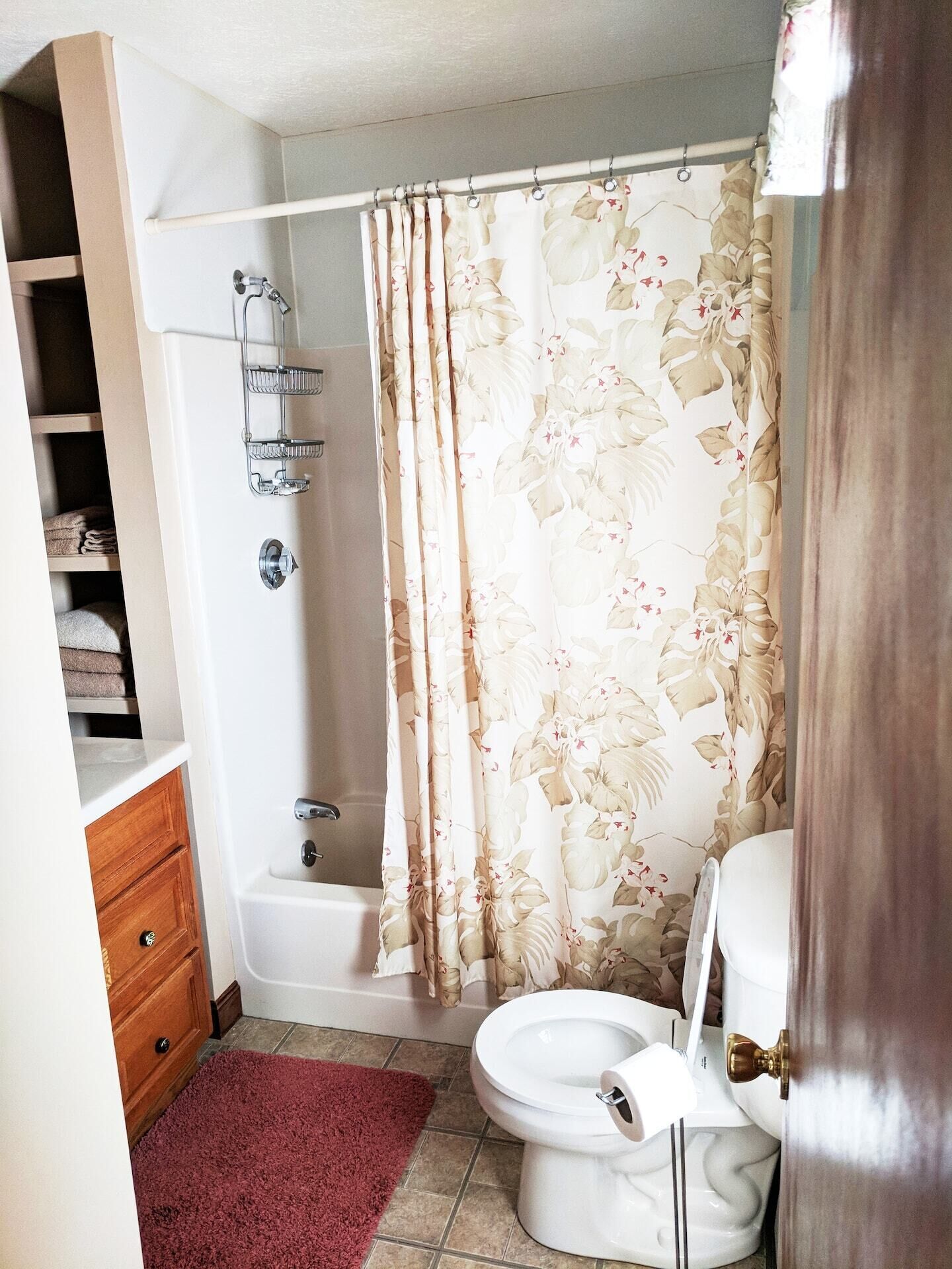 Een badkamer met douchegordijn, toilet, badkuip en een plank met handdoeken.