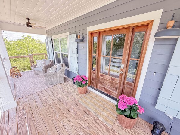 A wooden porch with wicker furniture, a door with glass panels, and a ceiling fan.