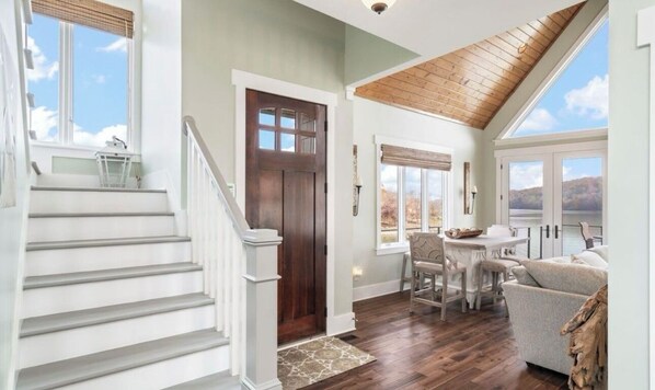 A spacious living area with a wooden staircase, a dining table, and a view of the outdoors.