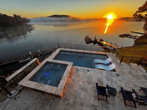 A swimming pool with lounge chairs and a hot tub, overlooking a lake with a sunset view. - Stunning VIEWS!  Lakefront Luxury w Saltwater Pool, Spa, & Deep-Water Dock (Rockwood)