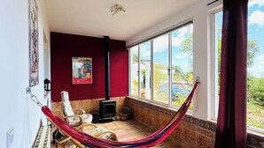Een kamer met een rode wand, een groot raam, een hangmat, een open haard en een betegelde vloer.