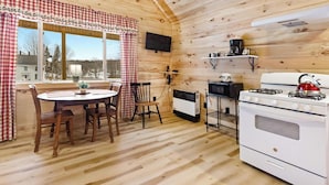 A cozy cabin-style room with a dining table, chairs, a stove, and a television.