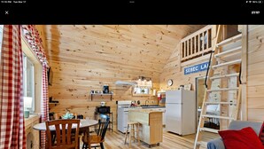 A cozy cabin interior with a dining area, kitchen, and a loft bedroom with a ladder.