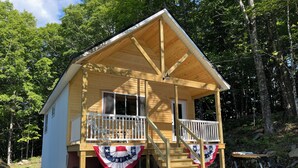 A wooden cabin with a porch, two windows, and a flag.