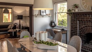 Et spiseområde med et marmorbord, grå polstrede stole, en hængende lysekrone og en murstenspejs.