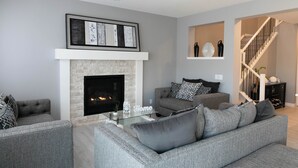 A modern living room with a fireplace, grey sofas, and a staircase. - AC, Scenic Cochrane Family Home (Cochrane)