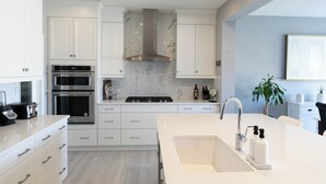 A modern kitchen with white cabinetry, a central island with a sink, and built-in appliances. - AC, Scenic Cochrane Family Home (Cochrane)