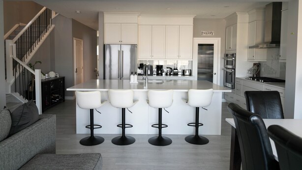 A modern kitchen with a central island, bar stools, and a dining area with a table and chairs. - AC, Scenic Cochrane Family Home (Cochrane)