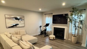Una sala de estar moderna con un sofá modular, una chimenea, un televisor y equipo de ejercicio.