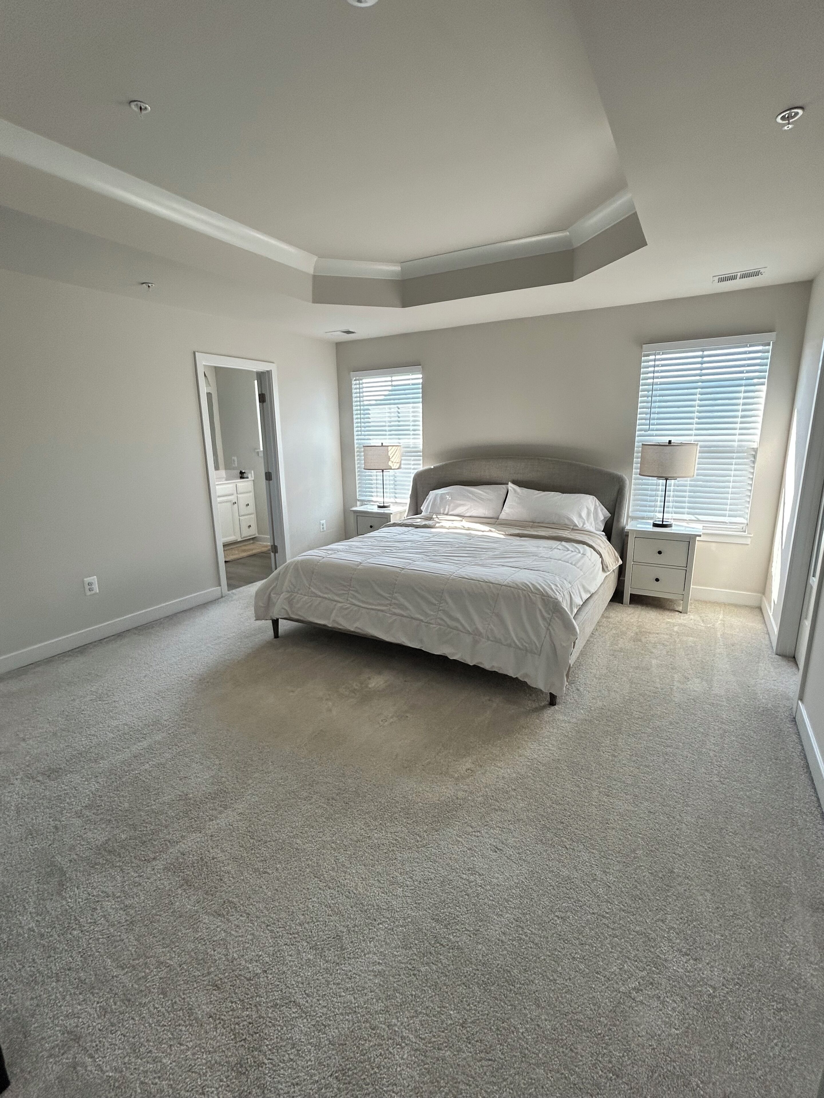 A bedroom with a large bed, two bedside tables, a mirror, and a window with blinds.