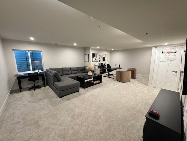 A modern living room with a sectional sofa, a desk, and a basketball hoop. - Modern and Cozy Home in Bel Air with a Home Office and Fireplace (Bel Air)