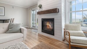 Een woonkamer met een open haard, een bank, een fauteuil en een vloerkleed.