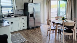 Een moderne keuken met witte kasten, een roestvrijstalen koelkast, een spoelbak en een eethoek met houten stoelen en een tafel.