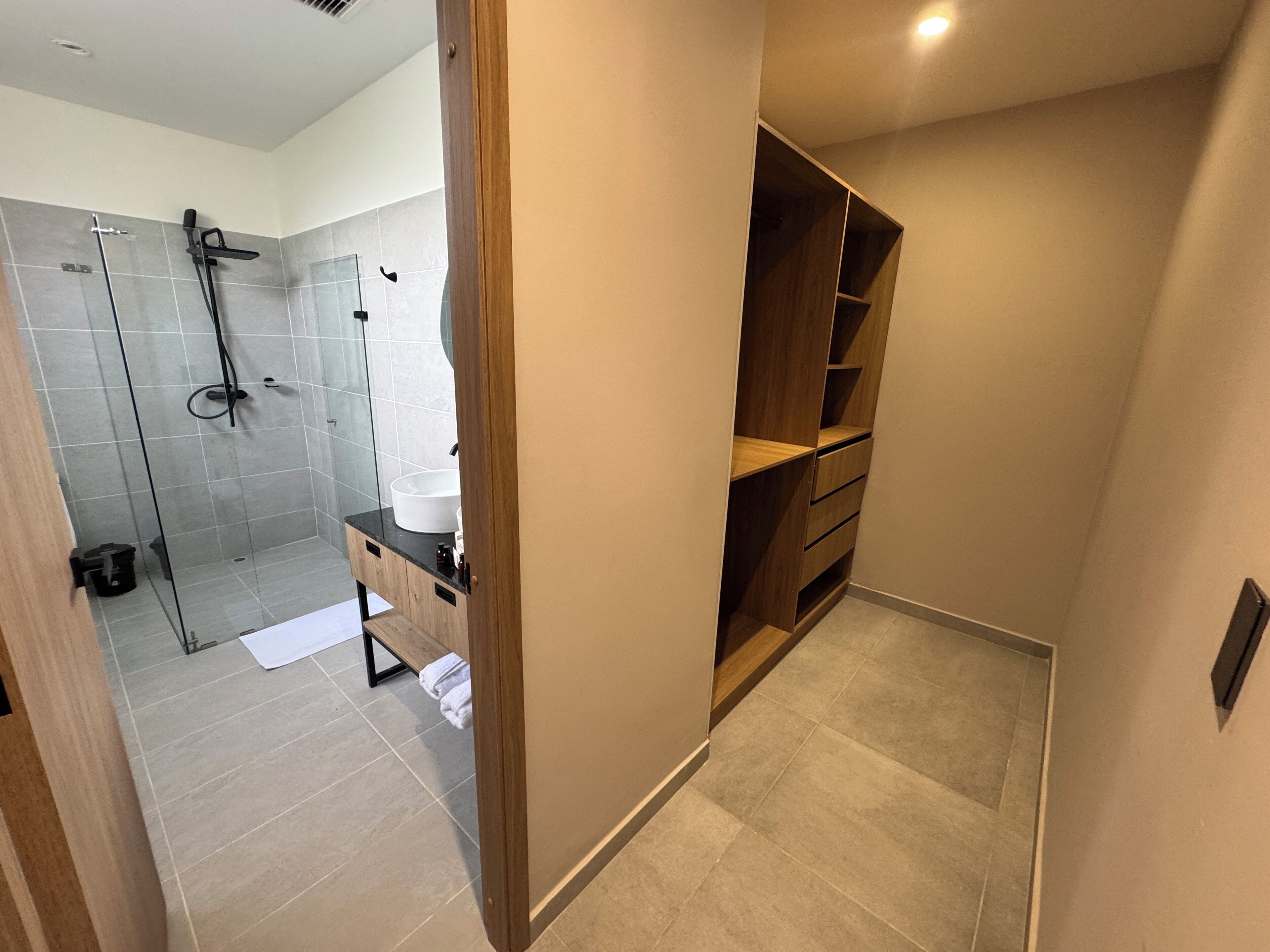 A modern bathroom with a glass shower enclosure, a wooden vanity, and a walk-in closet.