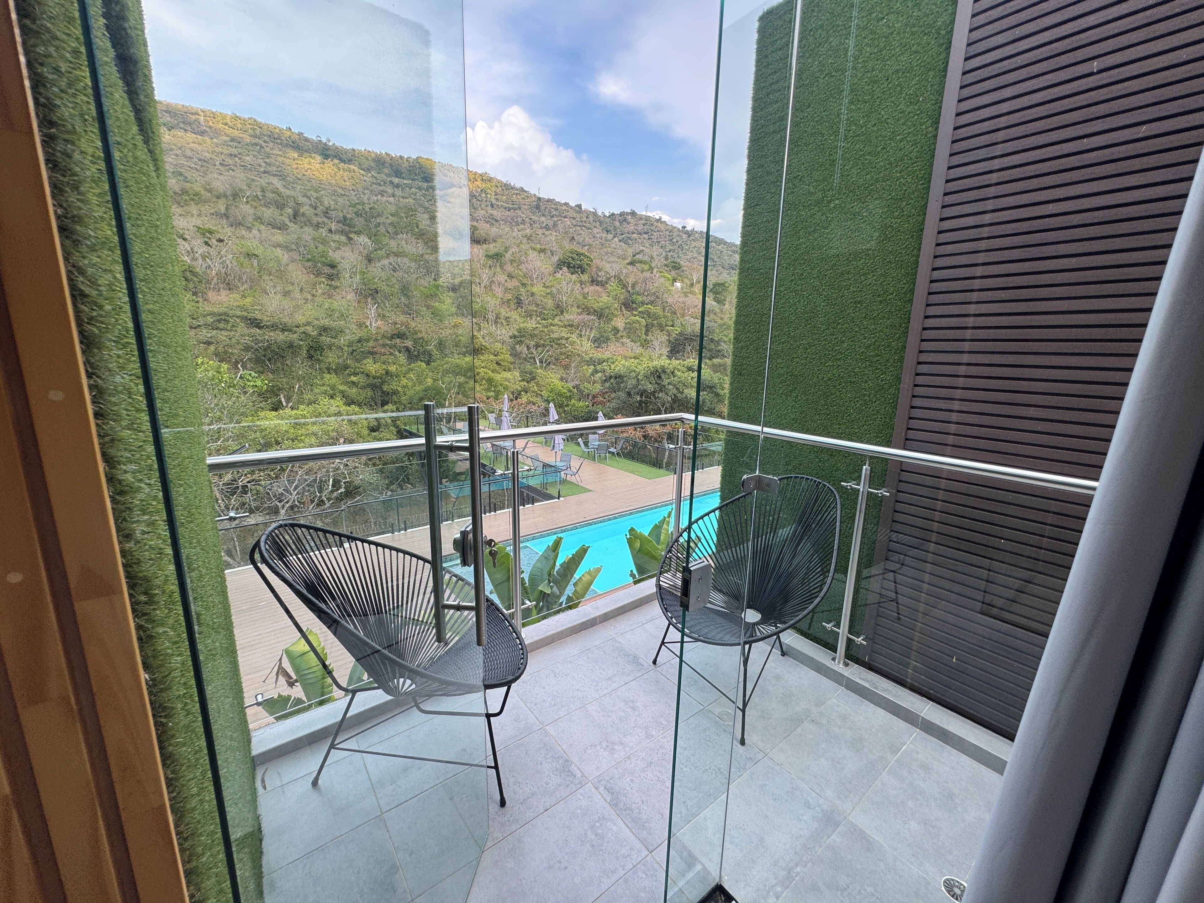 Un balcon avec deux chaises, une piscine et une vue sur un paysage vallonné.