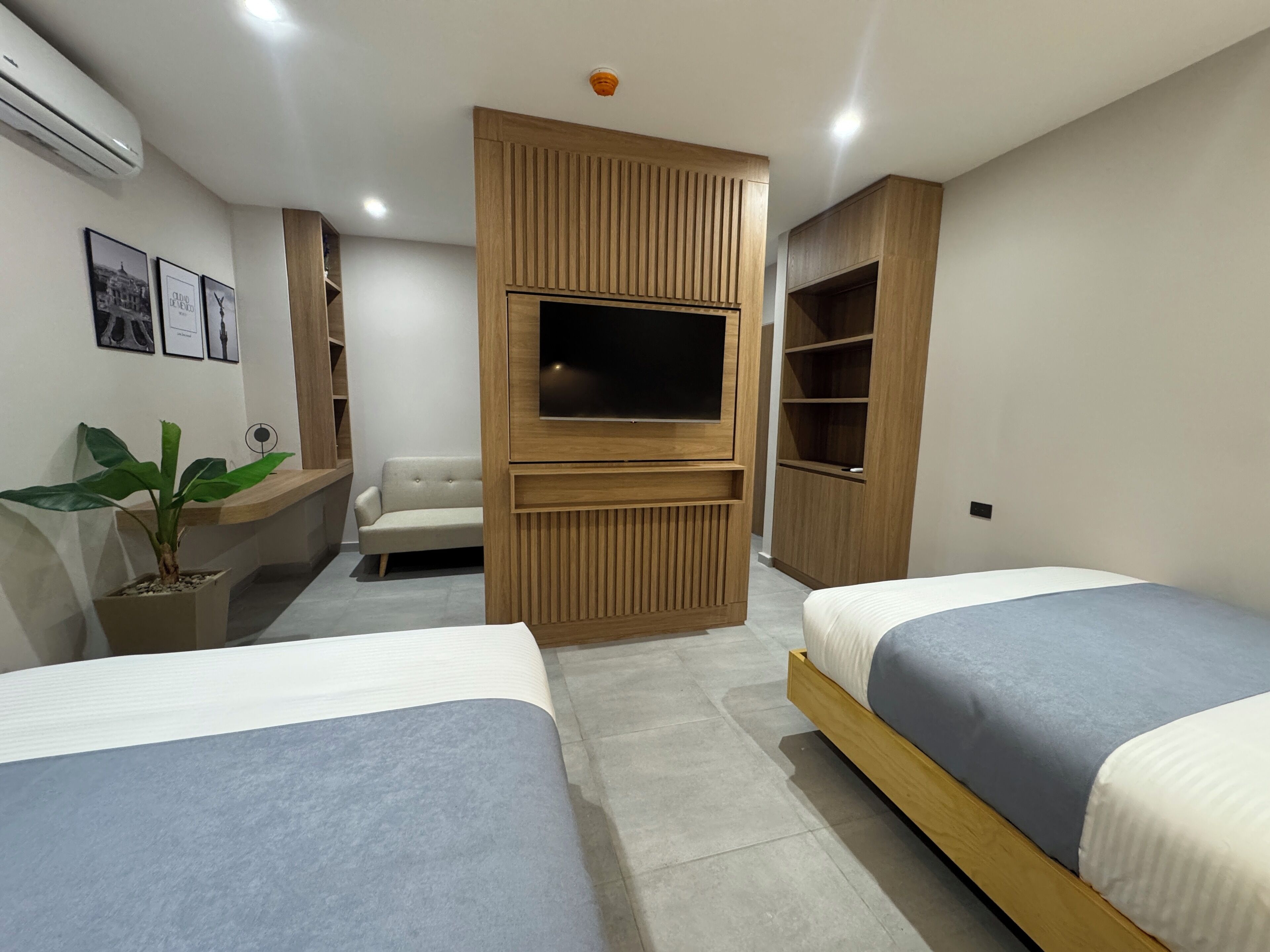 A modern bedroom with two beds, a TV, a sofa, and built-in shelving.