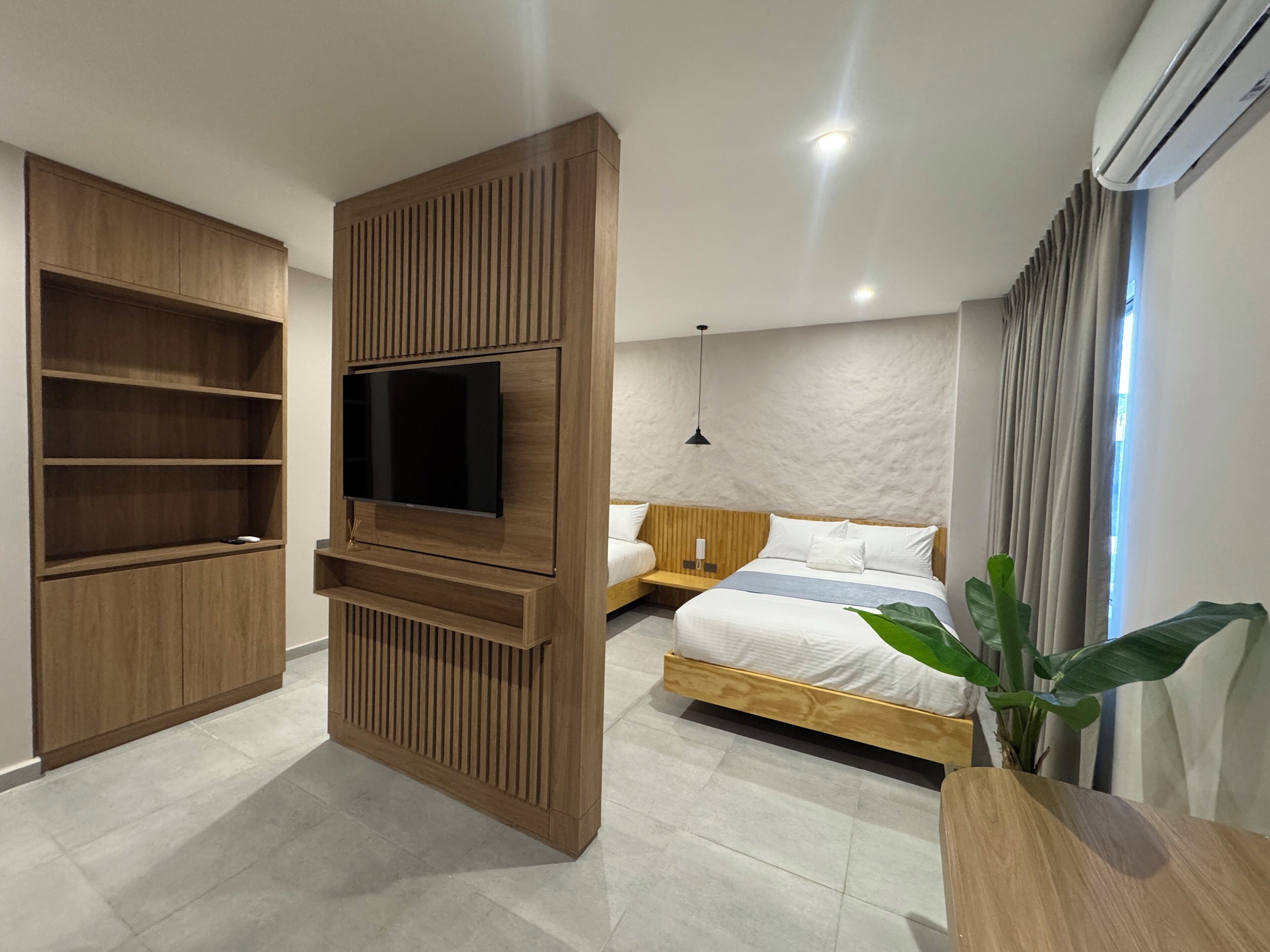 Une chambre moderne dotée d’un téléviseur intégré, d’étagères en bois, d’un lit avec un cadre en bois et d’une plante en pot.