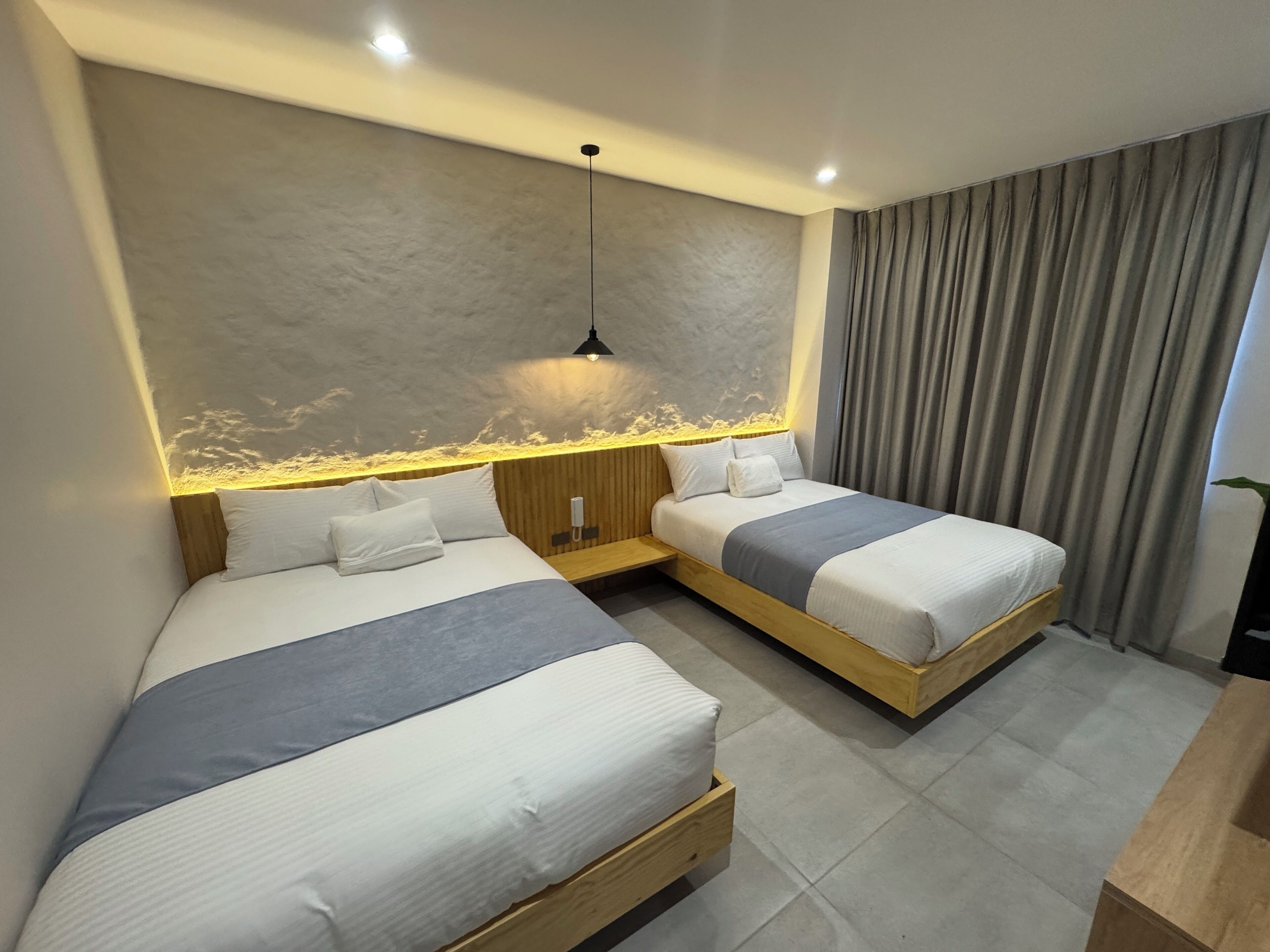 Habitación de hotel con dos camas, cabecera de madera, mesita de noche, teléfono y cortina.