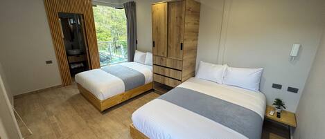 A modern bedroom with two beds, a wooden wardrobe, a small bedside table with a phone, and a view of greenery outside.