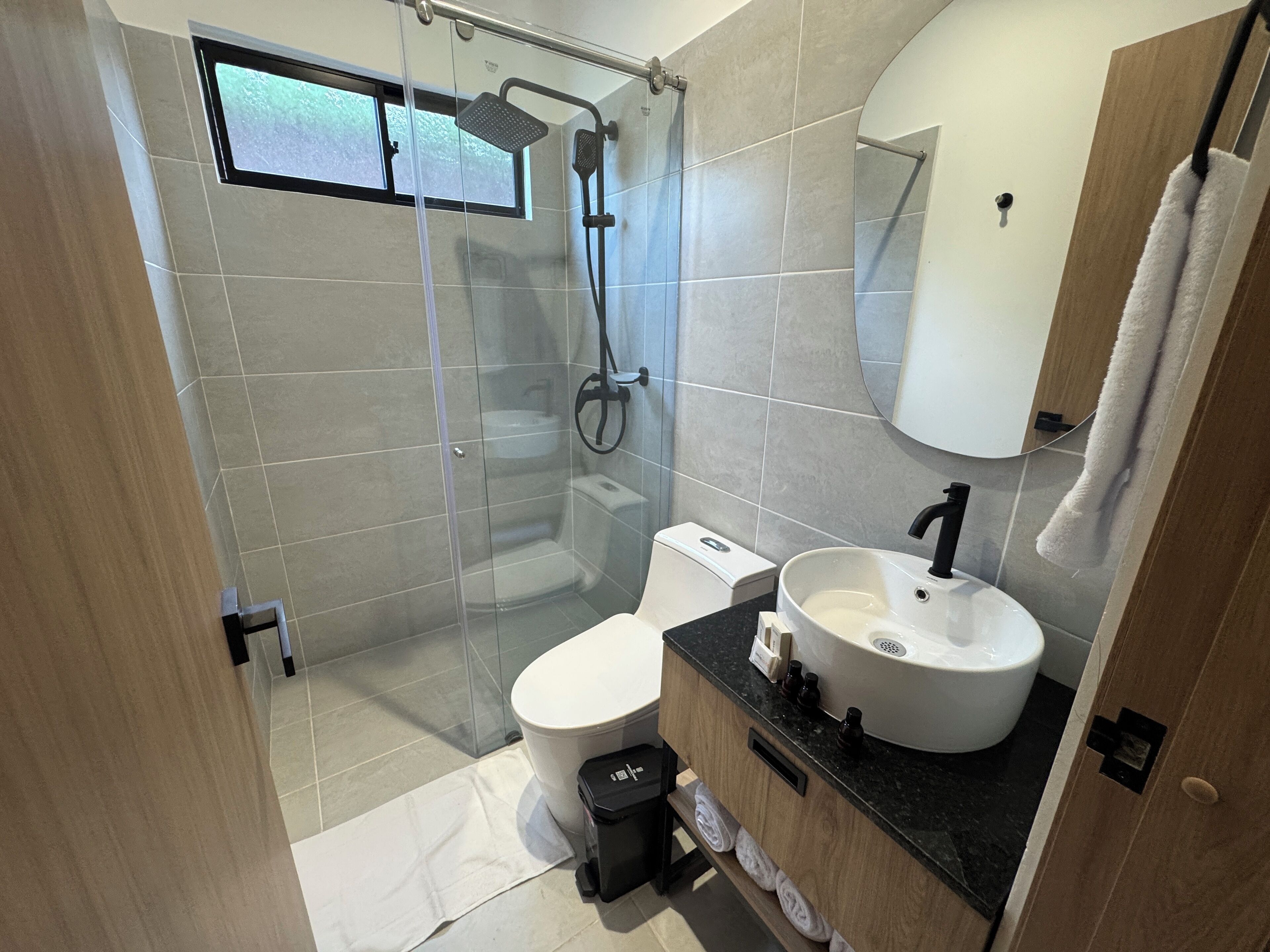 Un baño moderno con ducha de vidrio, inodoro blanco y lavamanos con encimera negra.