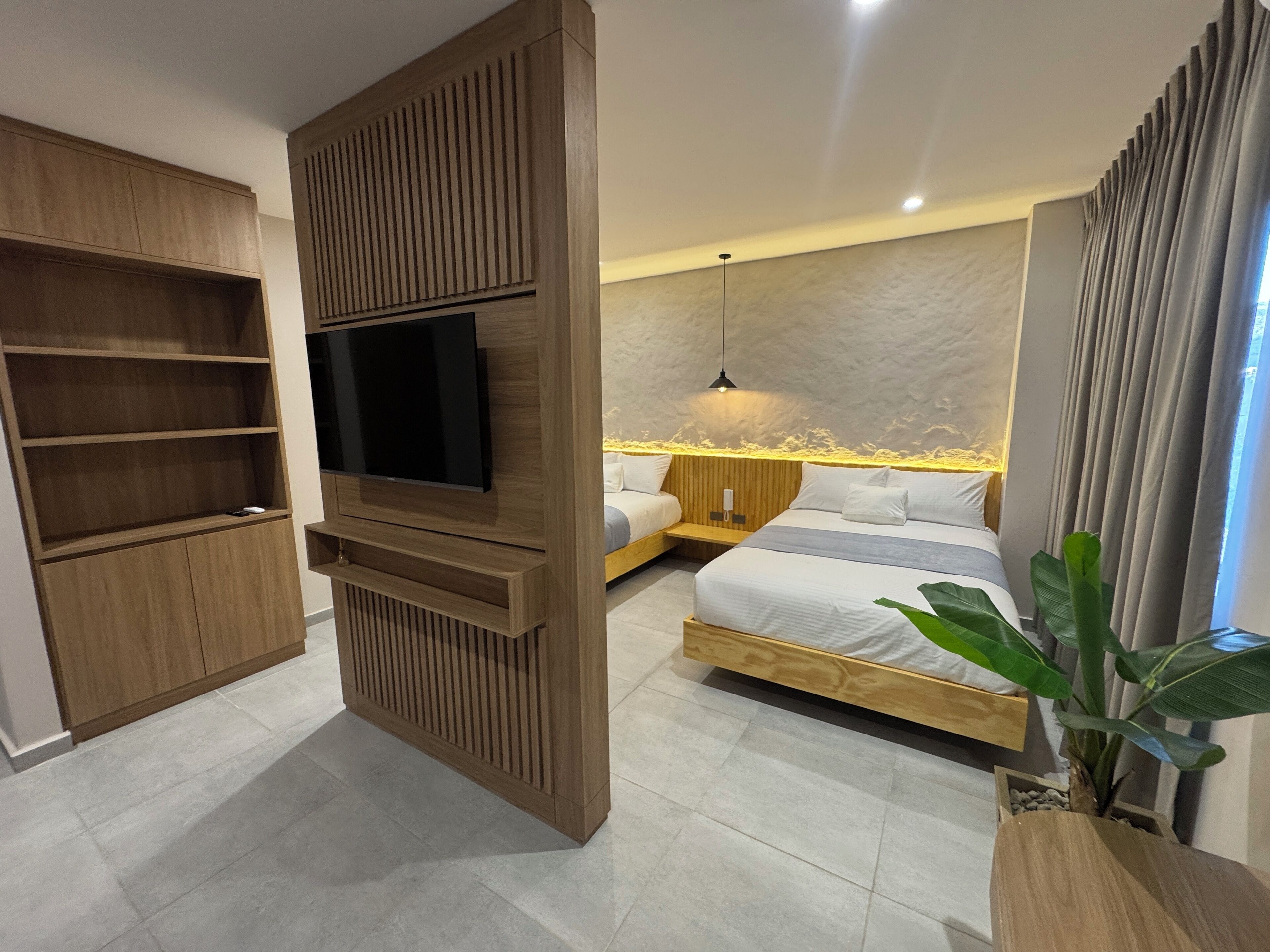 A modern bedroom with a built-in TV, a bed with a wooden headboard, a bedside table, and a potted plant.