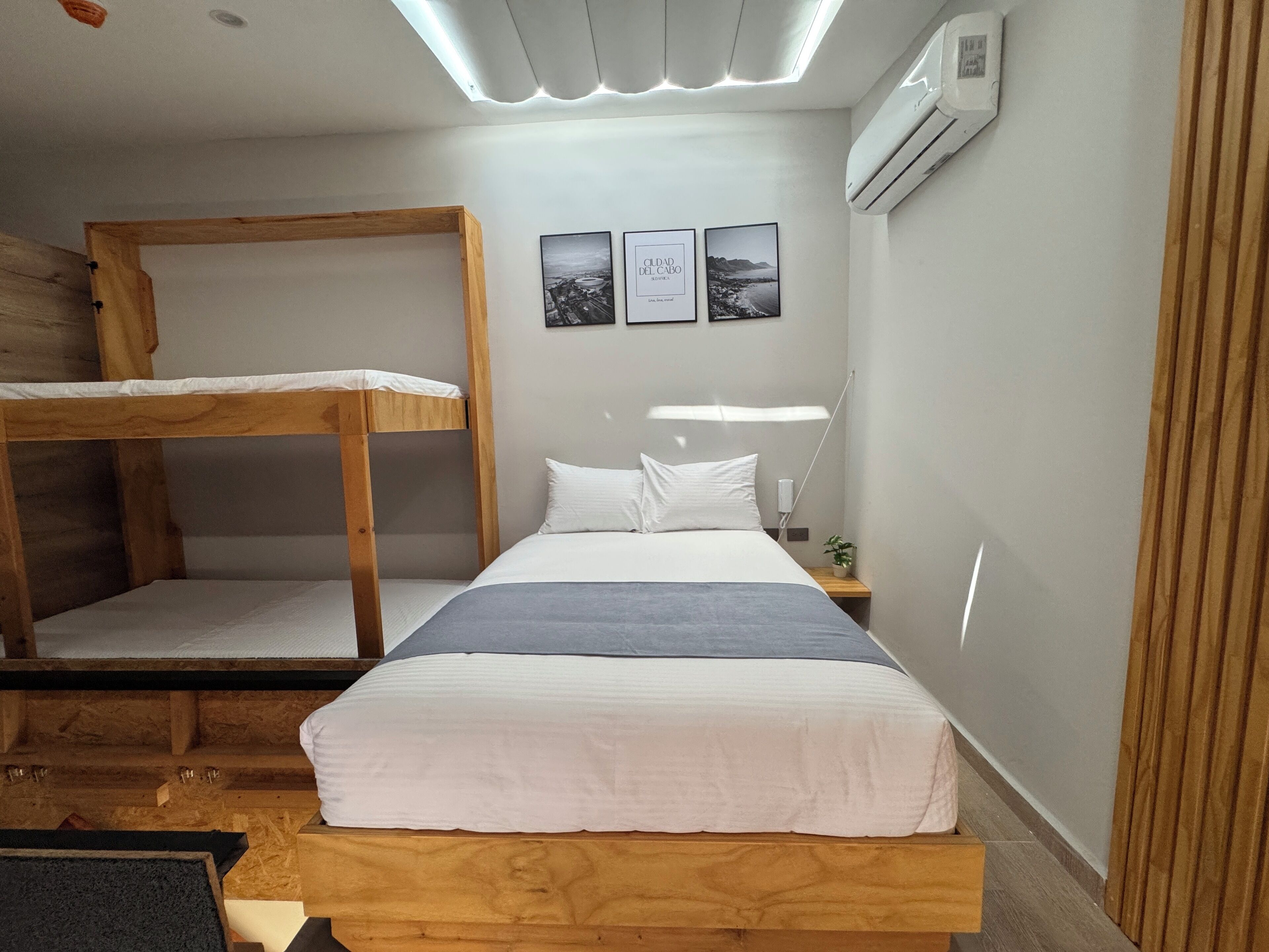 A bunk bed room with a desk and a nightstand. There are three framed pictures on the wall.