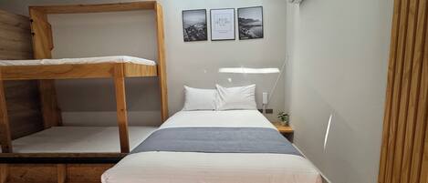 A bunk bed room with a desk and a nightstand. There are three framed pictures on the wall.