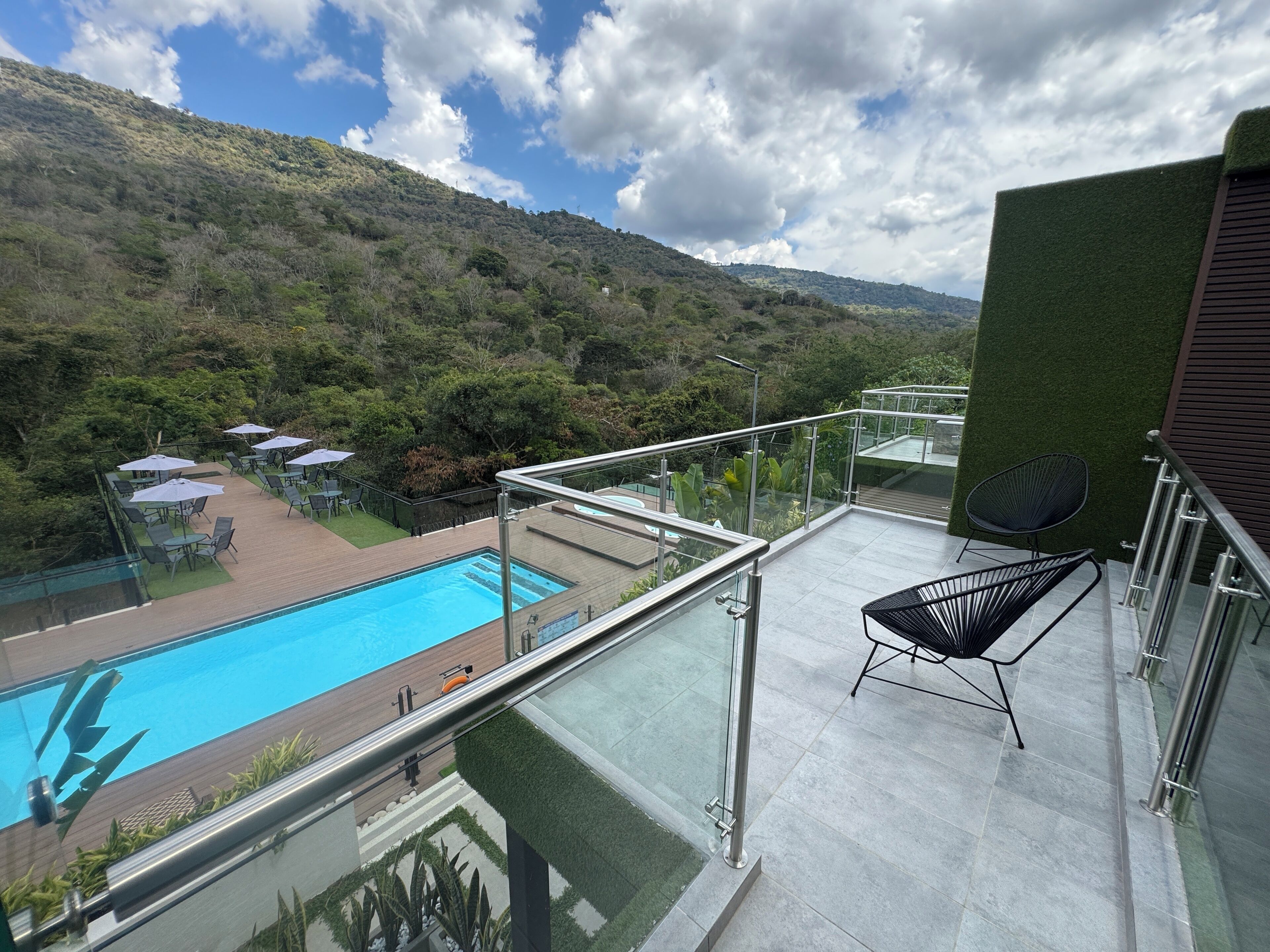 A balcony with a pool, outdoor seating, and a view of a hillside.