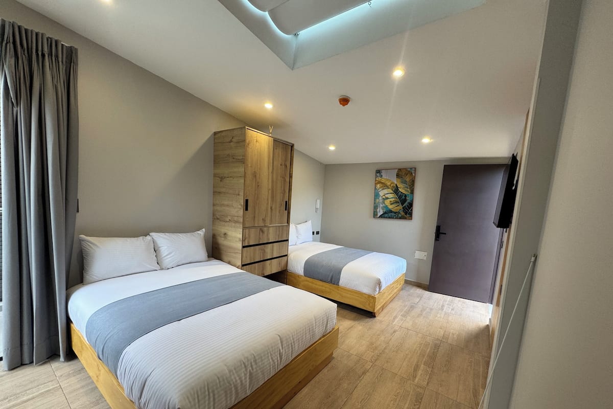 A modern bedroom with two beds, wooden wardrobe, and a ceiling light.