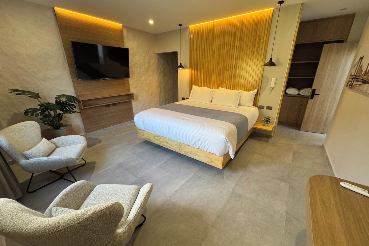 A modern bedroom with a large bed, a TV, a plant, and a desk.