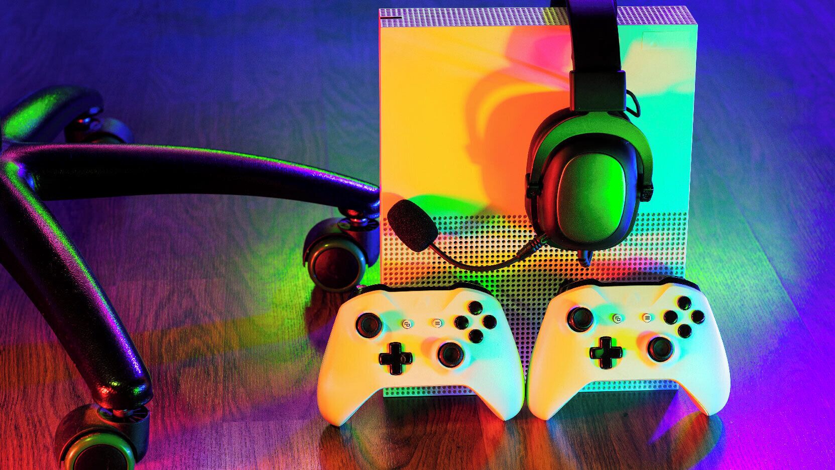 A pair of white gaming controllers with black buttons, a black headset, and a colorful LED light strip on a wooden surface.